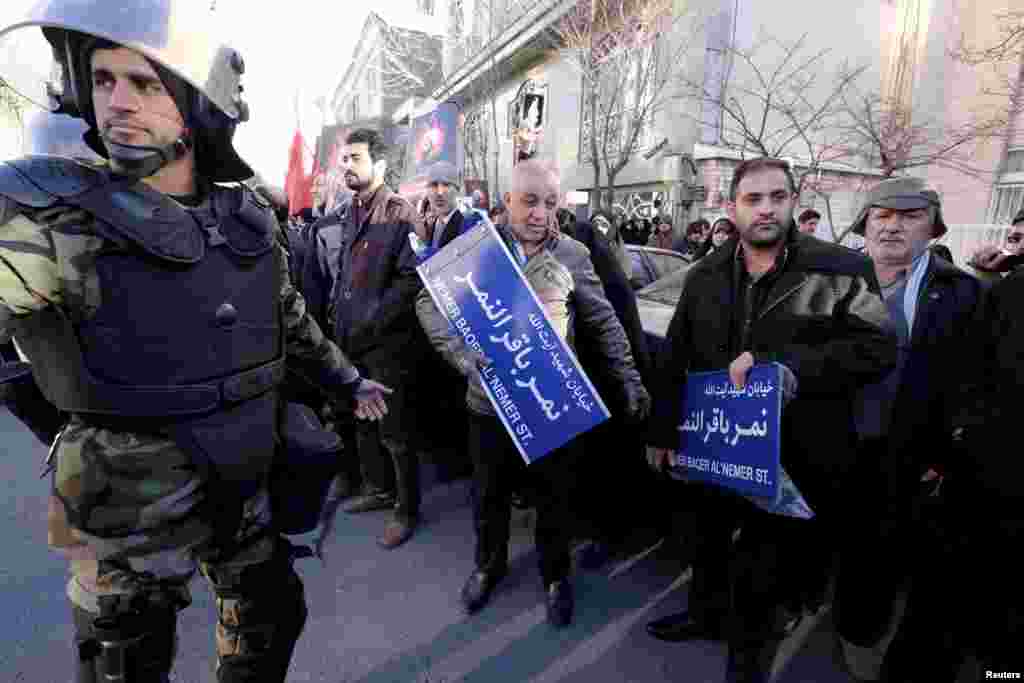 An Iranian riot policeman stands guard as protesters hold street signs with the name of Shi'ite cleric Sheikh Nimr al-Nimr during a demonstration condemning his execution in Saudi Arabia, outside the Saudi Arabian Embassy, in Tehran, January, 3, 2016.