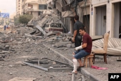 Palestinian men look at the destruction outside a damaged apartment building following Israeli airstrikes on Gaza City on October 10, 2023. (Photo by MAHMUD HAMS / AFP)