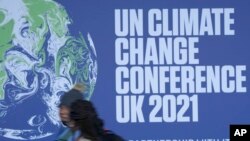 Moun pase bo kote yon banye ki tache sou yon miraj kote konferans COP a pral dewoule nan vil Glasgow, peyi Ekos.