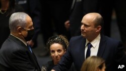 Israel's new prime minister, Naftali Bennett, shakes hands with outgoing prime minister, Benjamin Netanyahu, during a Knesset session in Jerusalem, June 13, 2021.
