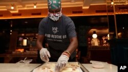 Sharon Holm, a volunteer from Food Rescue US, prepares cold cuts for sandwiches at Marcus Samuelsson's Red Rooster Restaurant during the new coronavirus pandemic, Monday, April 6, 2020, in the Overtown neighborhood of Miami. (AP Photo/Lynne Sladky)