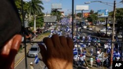 FILE - An individual watches from above as protestors march below during an anti-government protest in Managua, Nicaragua, Aug. 11, 2018. 