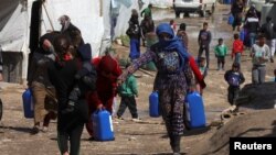 FILE - Syrian refugees walk as they carry containers at a tent settlement in Lebanon's Bekaa Valley, March 12, 2021. 