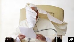 Le visage du pape François couvert par un pan de sa soutane soufflé par le vent pendant qu'il lit un discours durant une audience générale à la place St Pierre, au Vatican, mercredi 15 octobre, 2014.