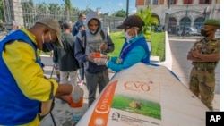 FILE - Locals, some wearing masks, have their bottles filled with a herbal extract they believe will protect them from COVID-19, in Antananarivo, Madagascar, April 23, 2020. 