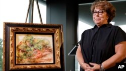 Sylvie Sulitzer, a delicatessen owner from the south of France, stands with a Renoir painting that was returned to her in a reparation ceremony at a news conference, Wednesday, Sept. 12, 2018, in New York. 