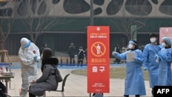 Seorang anggota staf medis (kiri) yang mengenakan alat pelindung mengambil sampel dari seorang pengunjung untuk menguji virus corona Covid-19 di stasiun pengujian sementara di luar Balai Kota di Seoul pada 23 Desember 2020. (Foto: AFP)