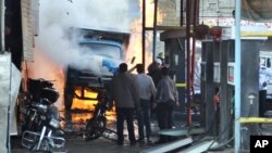 Foto yang dirilis oleh kantor berita SANA ini menampakkan warga Suriah yang sedang mengamati truk yang sedang terbakar akibat dua ledakan bom di Jermana, Damaskus, Suriah (28/11).