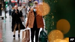 Seorang perempuan, yang mengenakan masker untuk menjaga diri dari infeksi COVID-19, membawa beberapa kantong belanjaan ketika berjalan melalui Oxford Street di London, pada 27 Desember 2021. (Foto: AP/David Cliff)
