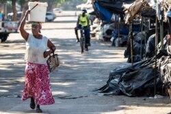 A vendor carries fresh produce as police officers disperse people from a vegetable market in Bulawayo, Zimbabwe, March 31, 2020, on the second day of a lockdown to curb the spread of the coronavirus.