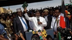 FILE - Opposition leader Raila Odinga, center, accompanied by lawyer Miguna Miguna, center-left, and others, holds a Bible aloft after a mock "swearing-in" ceremony at Uhuru Park in downtown Nairobi, Kenya, Jan. 30, 2018.