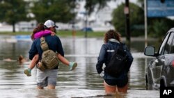 Don Noel carries his daughter Alexis, 8, with his wife Lauren, right as they walk through a flooded roadway to check on their boat in the West End section of New Orleans, June 21, 2017.