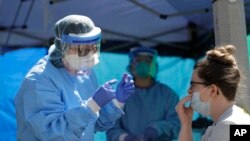 Tina Nguyen, left, a nurse at at the International Community Health Services clinic in Seattle's International District, takes a nose swab sample from Mindy Balk, an ICHS employee, during walk- and drive-up testing for COVID-19, Friday, May 15, 2020. (AP Photo/Ted S. Warren)