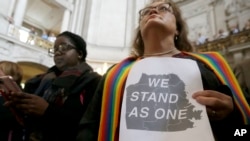 FILE - The Rev. Annie Steinberg-Behrman, right, provisional pastor with Metropolitan Community Church, holds a sign while listening to speakers at a meeting at City Hall in San Francisco to reaffirm the city's commitment to being a sanctuary city, Nov. 14, 2016.