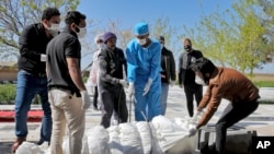 Men, some in protective gear, bury a coronavirus victim at a cemetery outside Tehran, Iran, March 30, 2020.