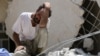 FILE - A man looks on as Syrian civil defense workers look for survivors under the rubble of a collapsed building following reported airstrikes in the rebel-controlled neighborhood of Karm Homad in Aleppo, July 17, 2016.