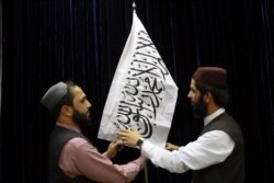Taliban officials arrange a Taliban flag, before a press conference by Taliban spokesman Zabihullah Mujahid, at the Government Media Information Center, in Kabul, Afghanistan, Aug. 17, 2021.