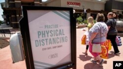 FILE - Shoppers carry their bags past a hand-sanitizing station at the Village Pointe shopping mall in Omaha, Neb., June 16, 2020. 