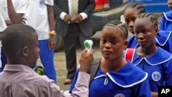Un enseignant de l'école libérien (à gauche) prélève la température des élèves qui arrivent pour les cours du matin à l'école, dans le cadre des mesures de prévention contre Ebola au Lycée Harris BW à Monrovia, le 16 février 2015.