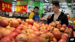 A woman wearing a uniform with the logo of an American produce company helps a customer shop for apples a supermarket in Beijing, Friday, March 23, 2018. China announced a $3 billion list of U.S. goods including pork, apples and steel pipe on Friday that it said may be hit with higher tariffs in a spiraling trade dispute with President Donald Trump that companies and investors worry could depress global commerce. (AP Photo/Mark Schiefelbein)