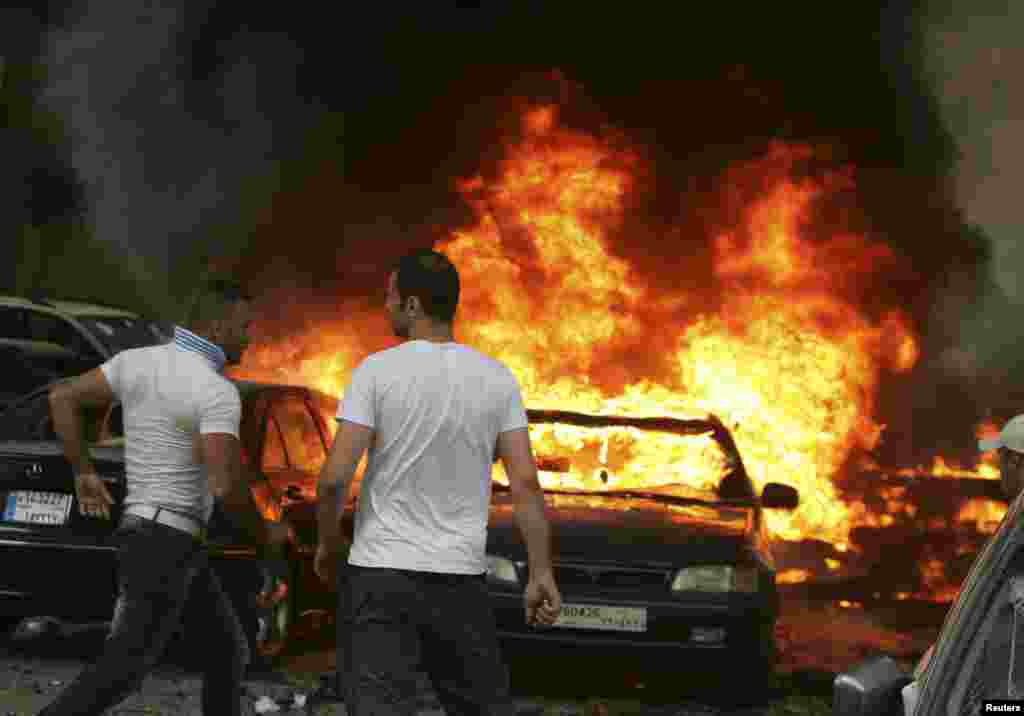 Men are seen near burning cars at the site of an explosion in Beirut's southern suburbs, July 9, 2013. 