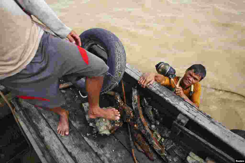 Seorang penyelam memegang topeng saat beristirahat di sebuah perahu kecil, setelah mengambil beberapa batu bara dan besi dari sebuah kapal yang tenggelam di Sungai Yangon, Burma