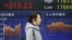 A woman walks by an electronic stock board of a securities firm in Tokyo, Feb. 1, 2016. Chinese stocks fell Monday after a weak manufacturing report. Other markets were mixed. 
