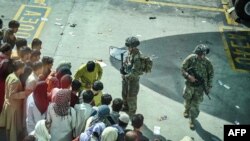 US soldiers stand guard as Afghan people wait at the Kabul airport in Kabul on August 16, 2021, after a stunningly swift end to Afghanistan's 20-year war, as thousands of people mobbed the city's airport trying to flee the group's feared hardline brand…
