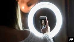 In this Feb. 28, 2018 photo, Matty Nev Luby holds up her phone in front of a ring light she uses to lip-sync with the smartphone app Musical.ly, in Wethersfield, Conn.