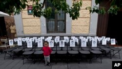 A child stands before a memorial made up of empty chairs bearing images of 43 missing students, set up to mark the nine-month anniversary of their disappearance, in Mexico City, June 27, 2015. 