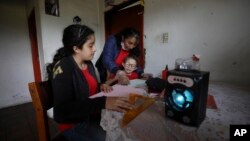 Fanny Mendez, right, mother of 14-year-old Marlene Beltran, left, and Felipe Beltrán, 5, helps her children study at home as they listen to an hour-long lesson broadcast by the Bacata Stereo radio station in Funza, Colombia, May 13, 2020. (AP Photo/Fernando Vergara)
