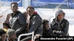 Wahamiaji wakiwa wameketi kwenye boti ya ulinzi wa bahari ya Italia wakisubiri kushuka katika bandari ya Palermo, baada ya kuokolewa Jumamosi, Aprili 18, 2015. Picha na shirila la habari la AP/Alessandro Fucarini. 