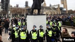 Des policiers se tiennent autour d'une statue lors d'une manifestation contre le confinement à Londres, en Grande-Bretagne, le 20 mars 2021.