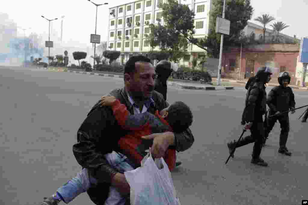 Seorang laki-laki menggendong anaknya berlari menjauhi gas air mata dalam bentrokan antara pasukan keamanan Mesir dan para pendukung presiden terguling Mohamed Morsi di Kairo. Para pendukung Morsi melakukan protes sporadis menentang referendum konstitusional minggu ini.