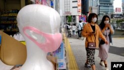 Para pejalan kaki melintas di depan boneka peraga dengan masker wajah di sebuah apotek di Tokyo, 31 Mei 2020. (Foto: AFP)