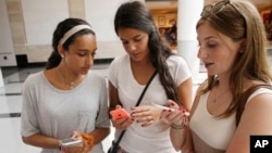 FILE - Teenage girls check their phones at Roosevelt Field shopping mall in Garden City, N.Y. A new study says social media can negatively impact the mental health of young people. 