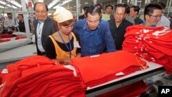 In this file photo taken on Aug. 30, 2017, Prime Minister Hun Sen, center, leans over a garment worker during a visit to a factory outside of Phnom Penh, Cambodia. 