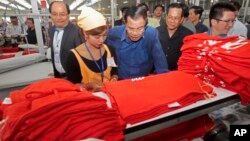 FILE - Prime Minister Hun Sen, center, leans over a garment worker during a visit to a factory outside of Phnom Penh, Cambodia, Wednesday, Aug. 30, 2017. Hun Sen embarked on a country-wide trip to visit the nation's factory workers to hear their hopes and concerns in person.