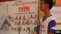 រូបឯកសារ៖ បណ្តាញ​យុវជន​សហគមន៍​ម្នាក់ ឈរ​នៅក្បែរ​ស្នាដៃ​សិល្បៈ ដើម្បី​លើកកម្ពស់ការយល់ដឹងពីបញ្ហាការចំណាកស្រុកដោយសុវត្ថិភាព ក្នុងពិធីបិទ​​សិក្ខាសាលាឆ្លុះបញ្ចាំងប្រចាំឆ្នាំរបស់បណ្ដាញយុវជនកម្ពុជា ទៅលើលទ្ធផល និងតួនាទីរបស់ពួកគេក្នុងការលើកកម្ពស់ចំណេះដឹងលើបញ្ហាការចំណាកស្រុកដោយសុវត្ថិភាព និងការការពារពីអំពើជួញដូរមនុស្សក្នុងប្រទេសកម្ពុជា នៅ​ថ្ងៃ​ទី​១១​ ខែ​មិថុនា ឆ្នាំ​២០១៥។ (នូវ​ ពៅលក្ខិណា/VOA)