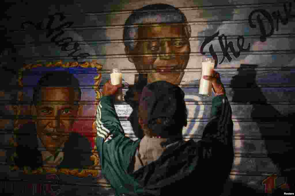 A man holds candles in front of a mural of former South African President Nelson Mandela and U.S. President Barack Obama in New York, Dec. 5, 2013.