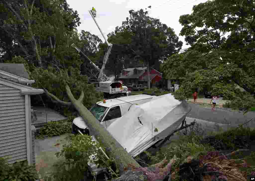 Sebuah mobil van dan perahu tertimpa pohon yang tumbang, sementara pekerja berusaha memperbaiki aliran listrik di Northfield, New Jersey.