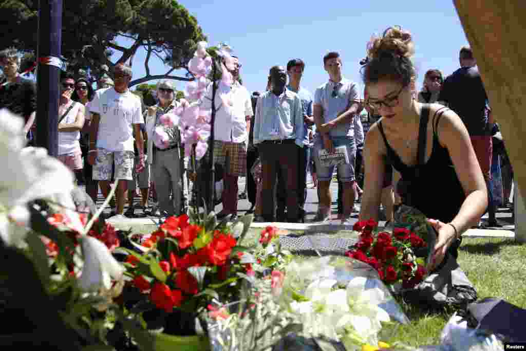A woman places a bouquet of flowers as people pay tribute near the scene where a truck ran into a crowd at high speed killing scores and injuring more who were celebrating the Bastille Day national holiday, in Nice, France, July 15, 2016. 