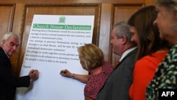 Britain's opposition Labour Party's shadow Chancellor John McDonnell, left, signs a cross-party declaration during an event with representatives of Britain's other pro-EU political parties, to discuss Brexit, in London, Aug. 27, 2019.