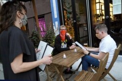 Owner Samantha DiStefano, left, prepares to hand menus to patrons and neighborhood regulars, Tuesday, Sept. 29, 2020, at her Brooklyn restaurant and bar in New York. Indoor dining opens Wednesday in New York, but at 25% capacity. "We're all a little…