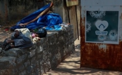 An Indian man sleeps next to a sign urging people to stay at home as a precaution against coronavirus in the premises of a hospital in Hyderabad, India, April 29, 2021.