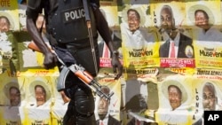 FILE - An armed Ugandan riot policeman is seen on patrol against the backdrop of campaign posters for long-time President Yoweri Museveni, as well as local members of Parliament, on a street in Kampala, Uganda, Feb. 17, 2016.