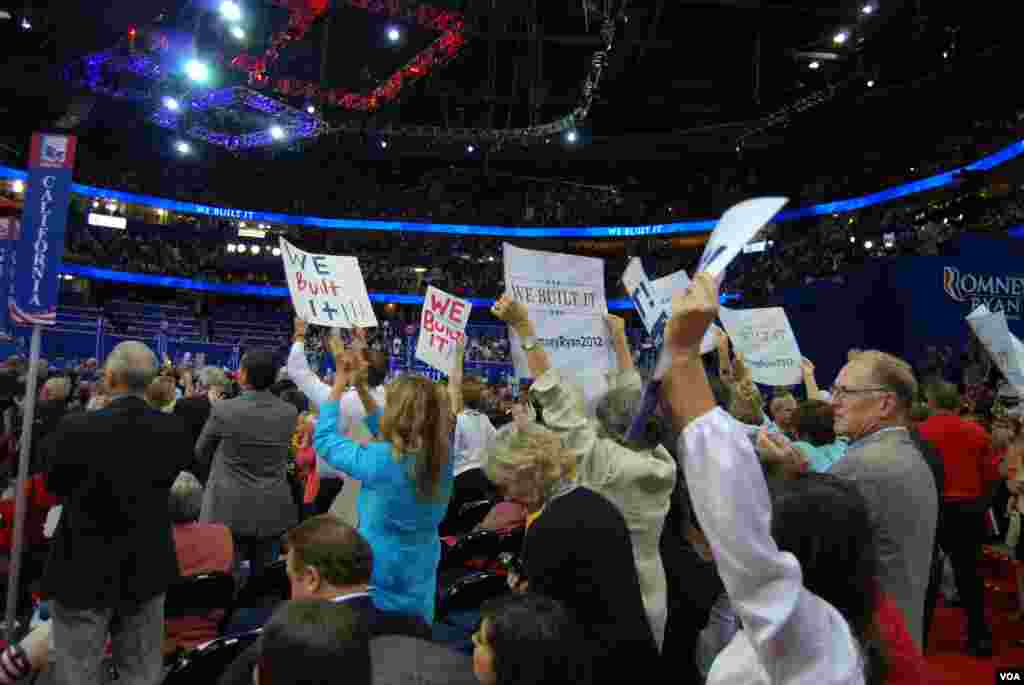 Para delegasi memegang poster &quot;We Built It&quot; sambil mendengarkan para pembicara di konvensi (28/8). (J. Featherly/VOA)