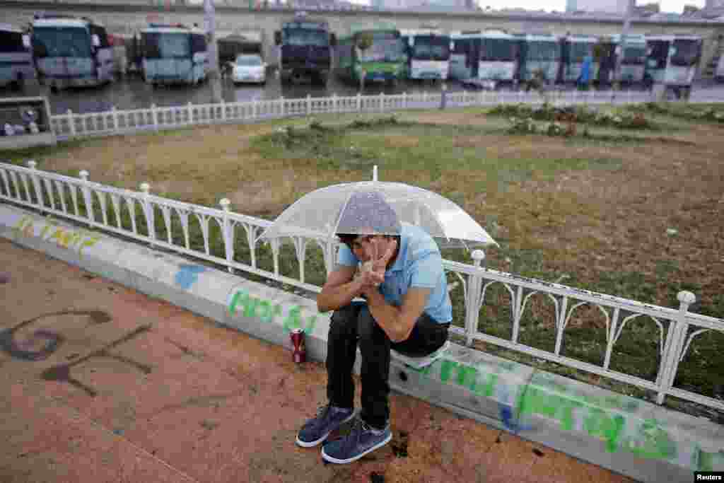 A protester makes the victory sign as he sits outside Gezi Park in front of riot police vehicles at Taksim Square, Istanbul, June 14, 2013.