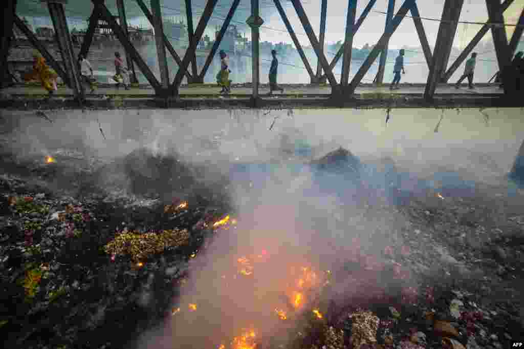 Pedestrians cross an iron bridge as smoke rises from a fire in a garbage dump below them near the Buriganga river in Dhaka, Bangladesh.