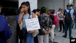 资料照片: 2024年2月5日一名妇女在阿根廷人力资本部长办公室外与其他人一起排队等待援助。标语牌上面西班牙语写着：“我是贝蒂，一名学生，我没有足够的食物”。 